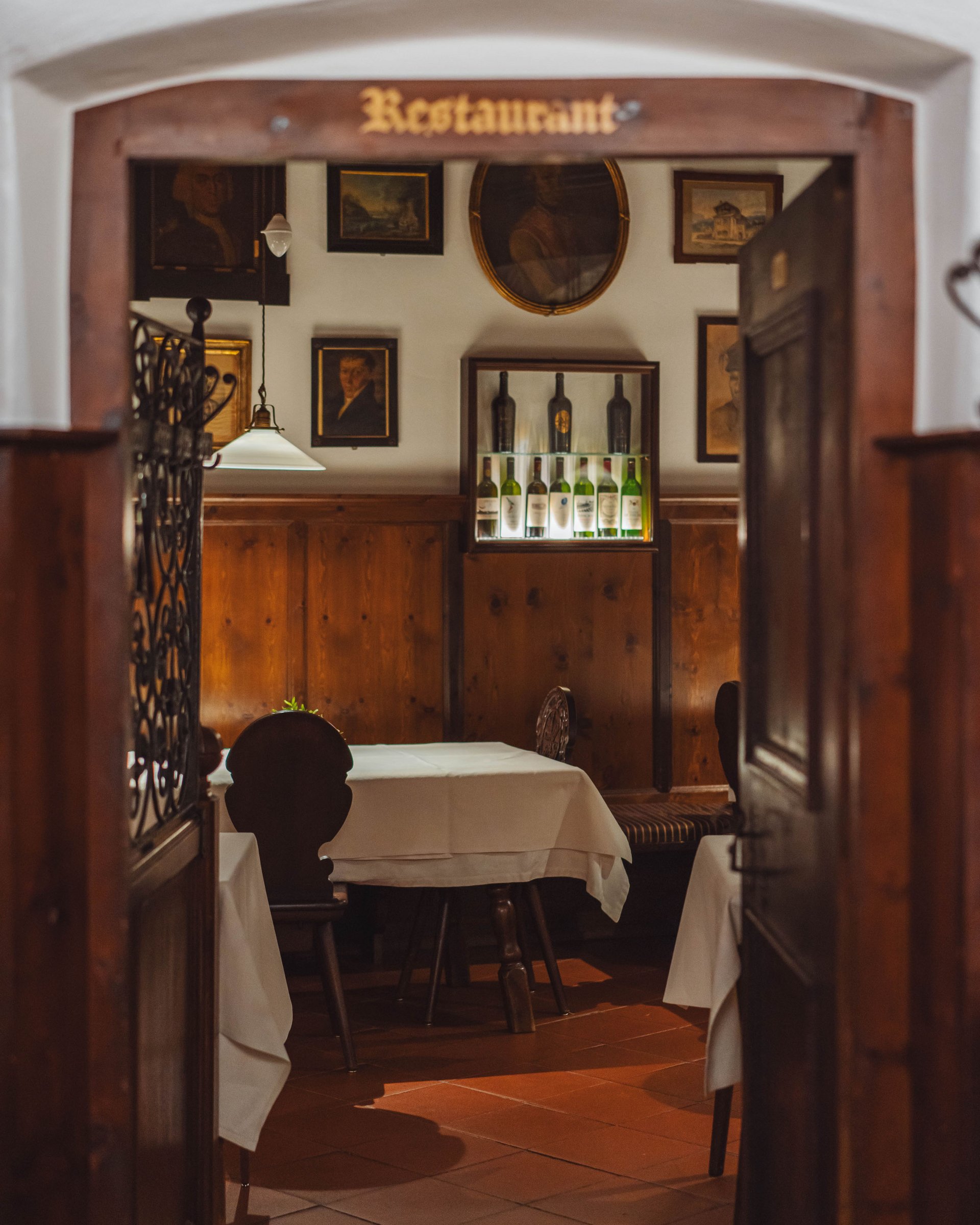 View through open door into rustic restaurant with wooden furniture and wine bottles