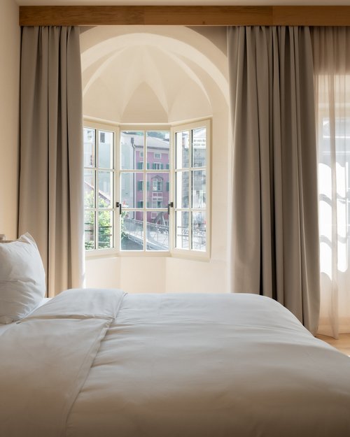 Bright bedroom with large bed, armchair, and open window overlooking colorful houses