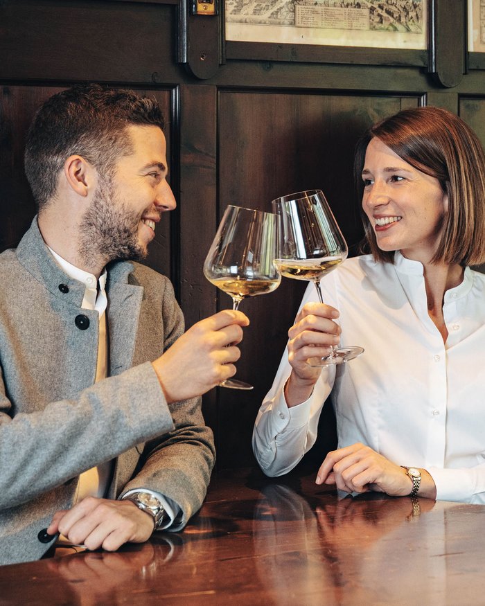 Man and woman clinking wine glasses seated at a wooden table