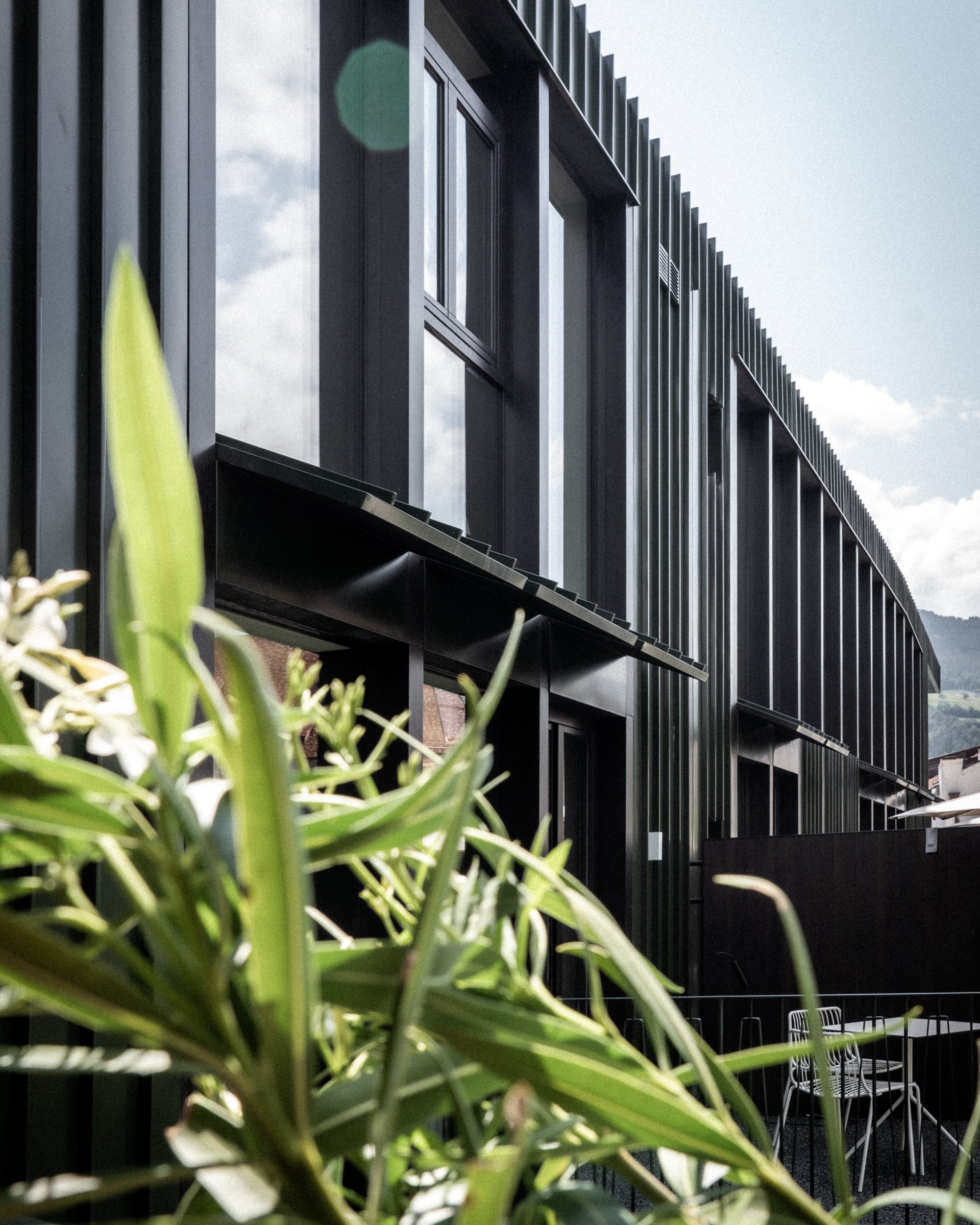 Moderne schwarze Gebäudefassade mit Pflanzen und Gartenmöbeln im Vordergrund