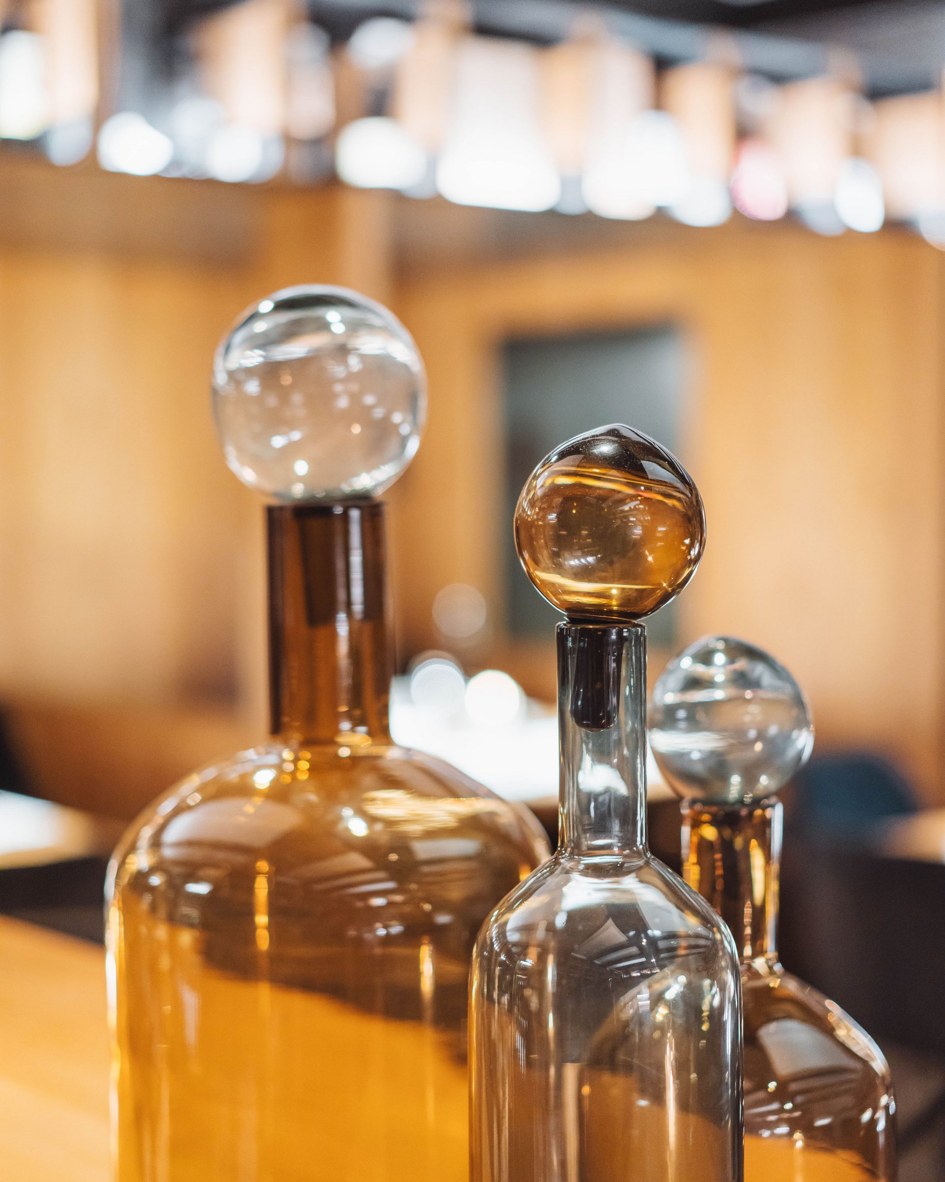 Three decorative glass bottles with spherical stoppers on wooden table