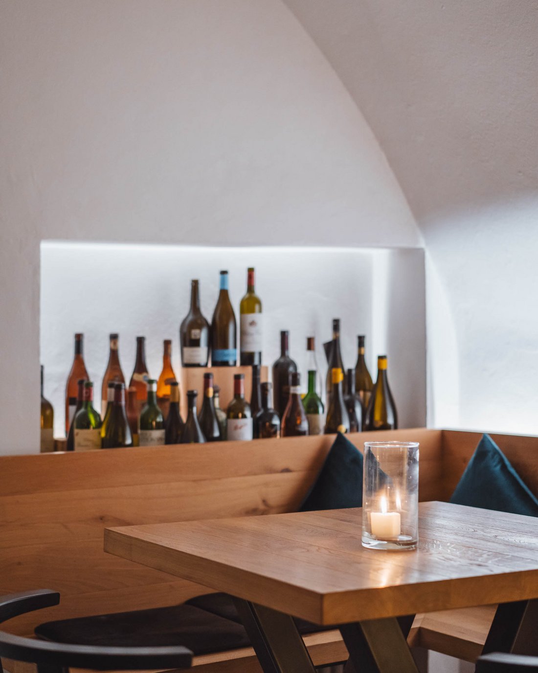 Gemütliche Ecke mit Holztisch, Kerze und Weinflaschen im Regal