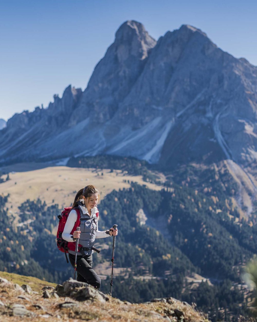 Woman hiking with backpack and poles in mountains under clear sky