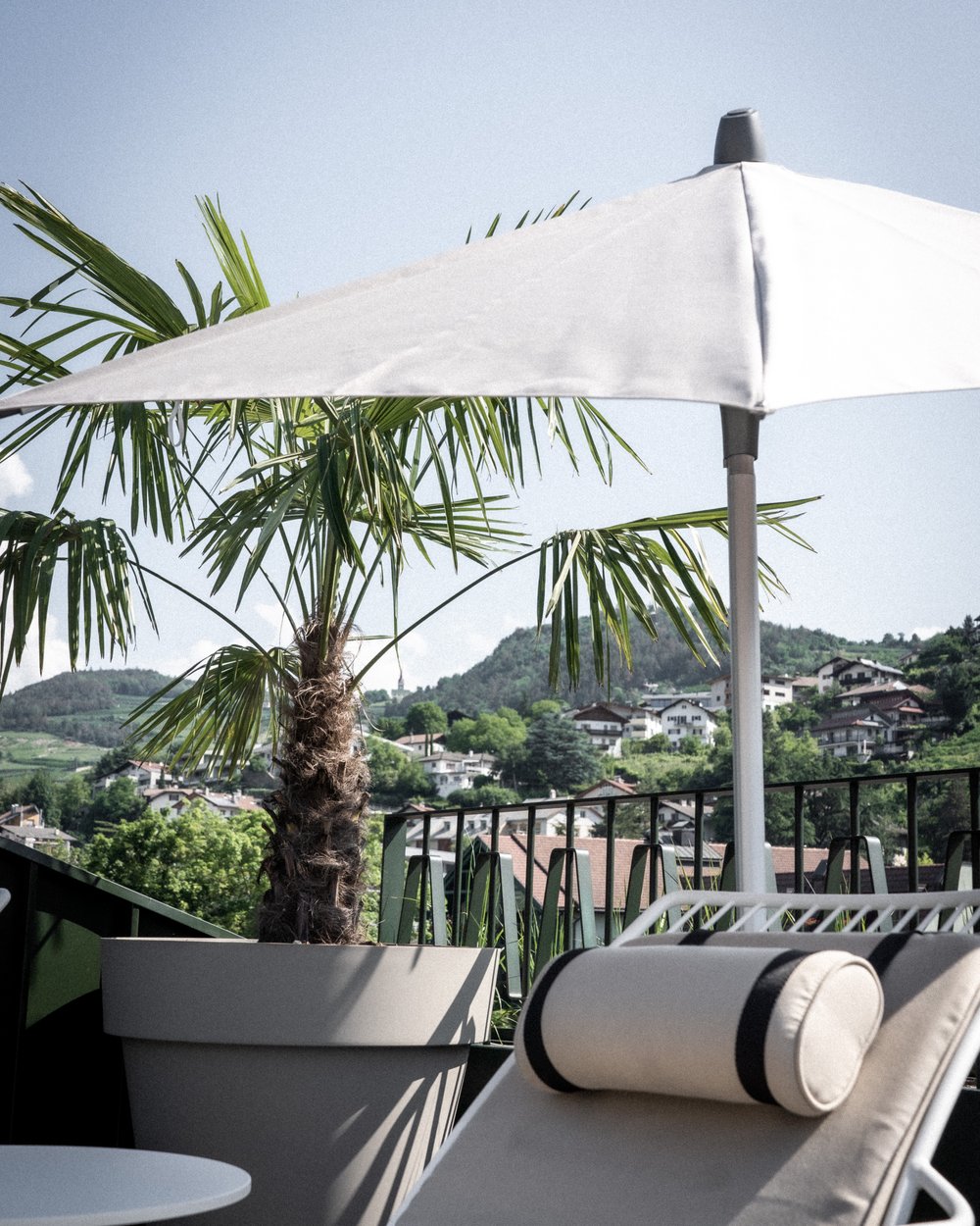 Liegestuhl und Sonnenschirm neben Topfpflanze auf Balkon mit Bergblick