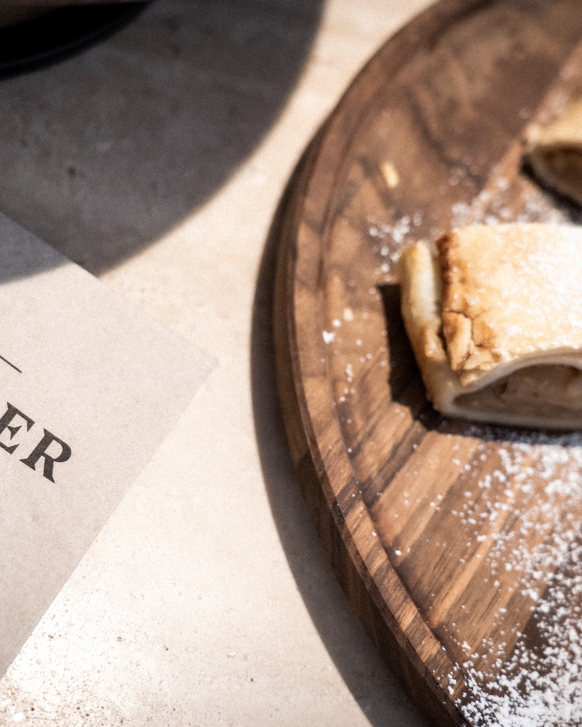 Apfelstrudelstücke auf Holzbrett neben ADLER Tagesbar Karte