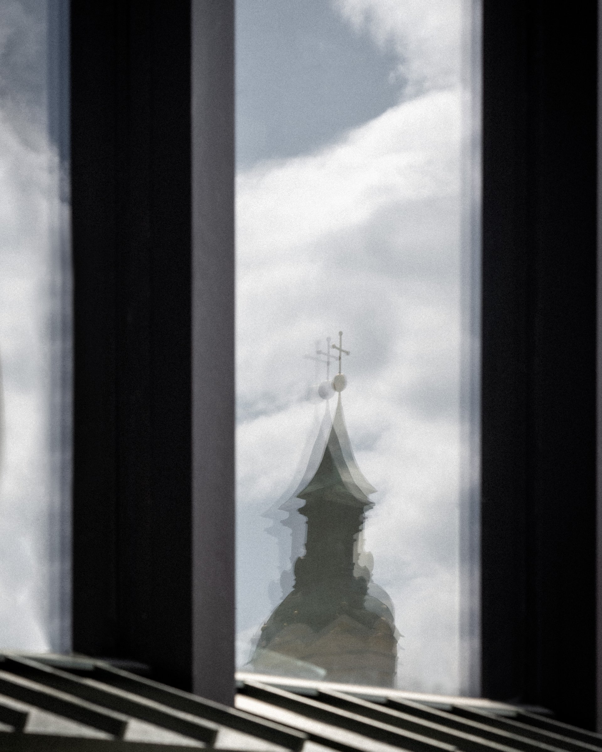 Spiegelung eines Kirchturms mit Wolken im Fenster