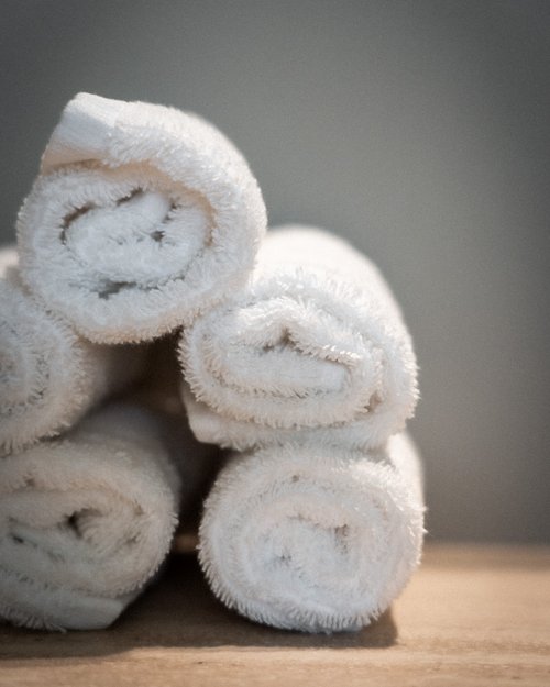 Vier sorgfältig gerollte weiße Handtücher auf einem Holztisch