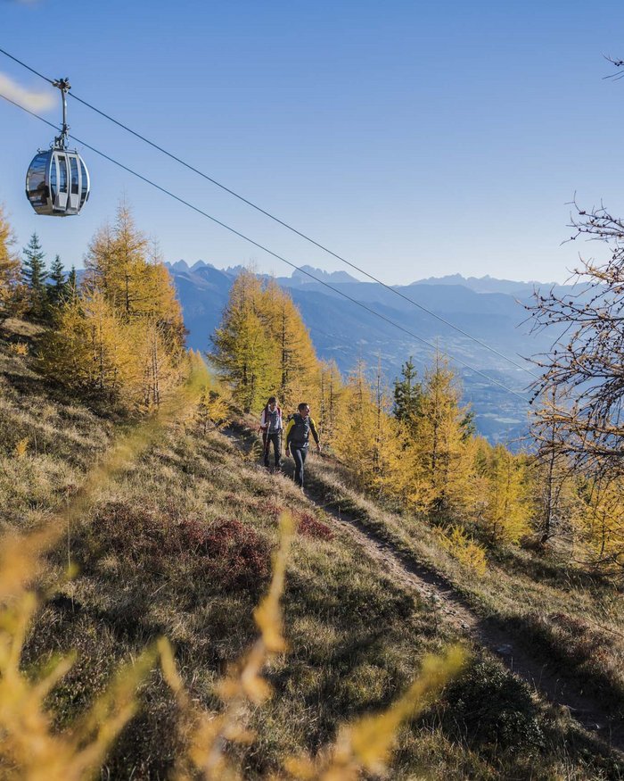 Zwei Wanderer auf einem Pfad in herbstlichem Wald mit Bergbahn in den Alpen