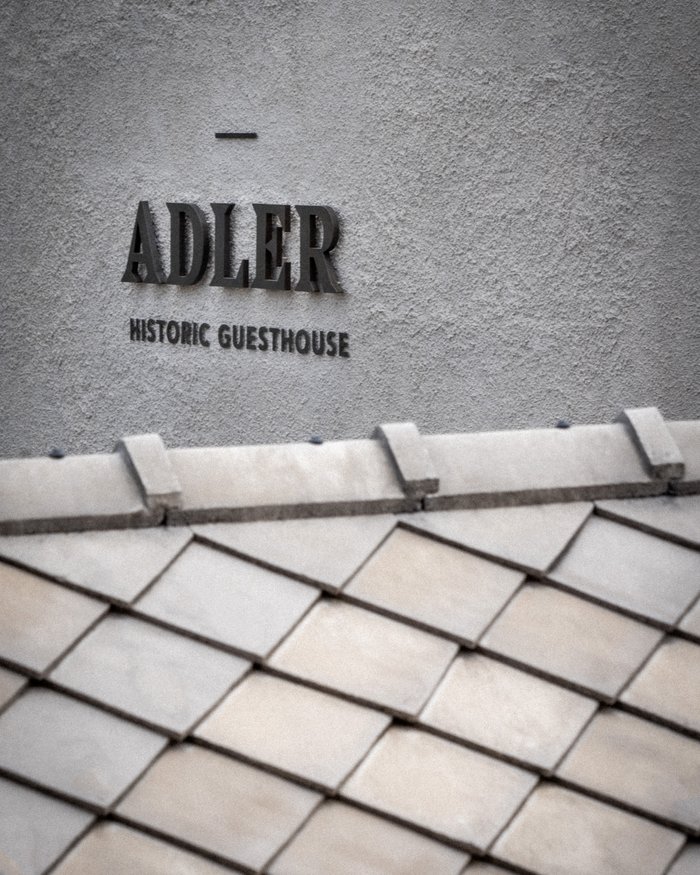 Schriftzug Adler Historic Guesthouse an grauer Wand über Ziegeldach