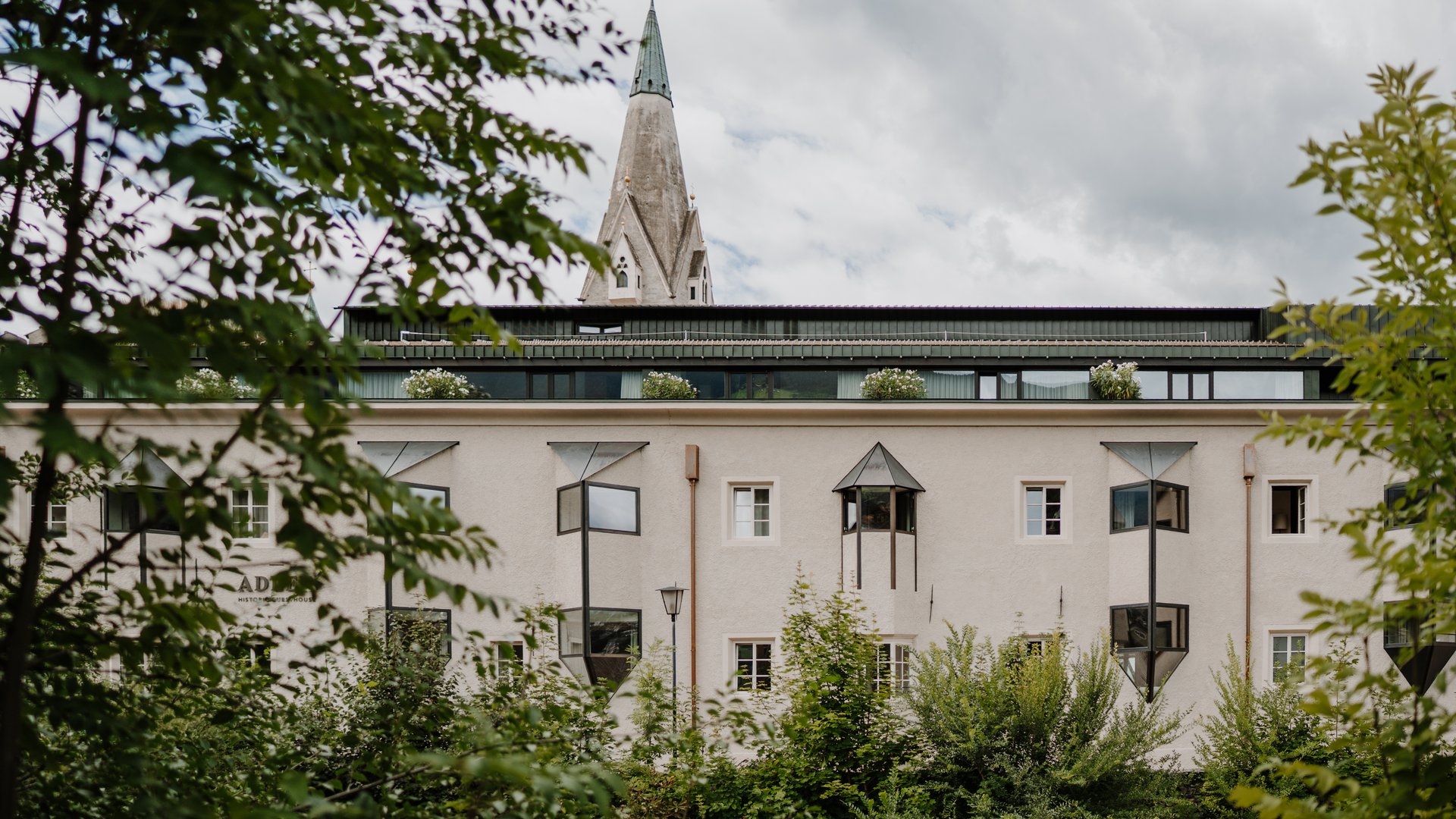 View of a historic building with a church tower behind trees