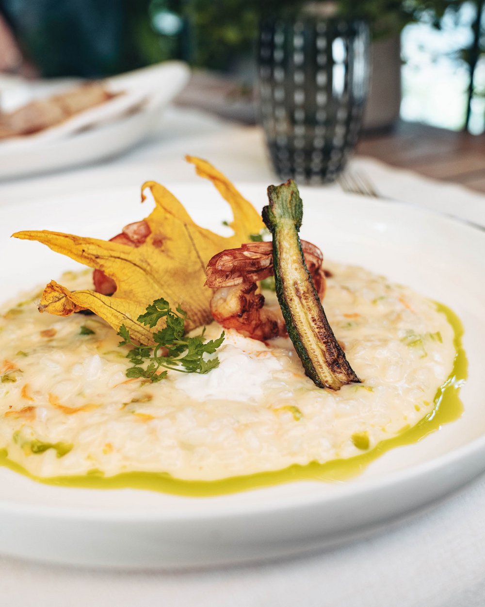 Ein Teller cremiges Risotto garniert mit Zucchini, Garnelen und essbaren Blüten