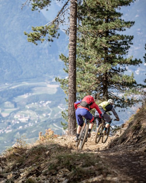 Zwei Mountainbiker fahren auf einem Bergtrail mit Talblick