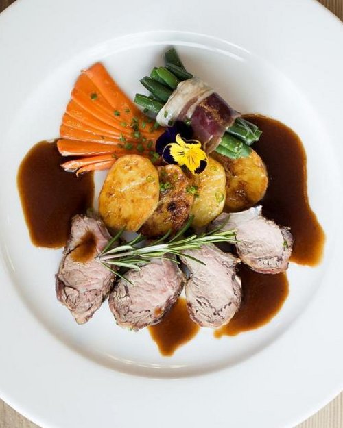 Gourmetgericht mit Fleisch, Kartoffeln, grünem Gemüse und Soße auf weißem Teller