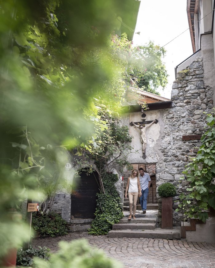 Couple walking down stone steps in old village with crucifix on wall