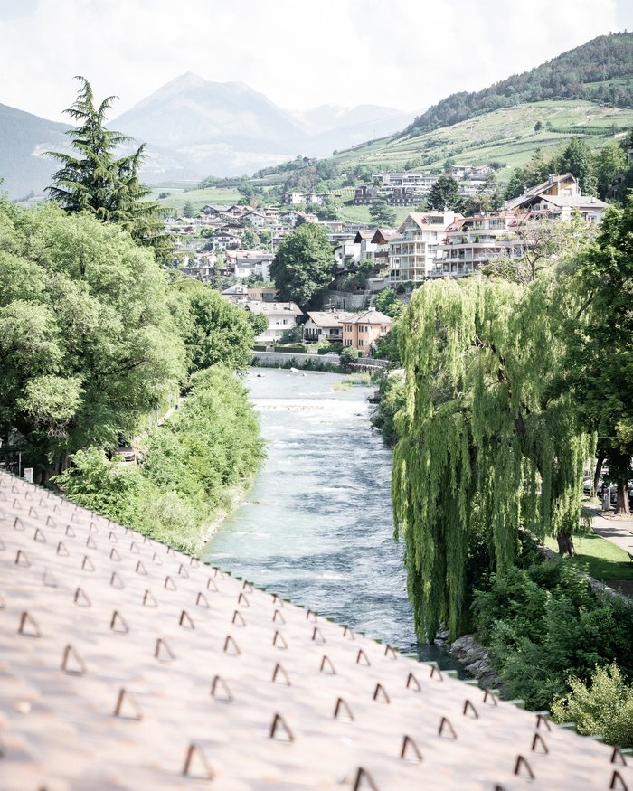 Fluss durch grüne Landschaft mit Häusern und Bergen im Hintergrund