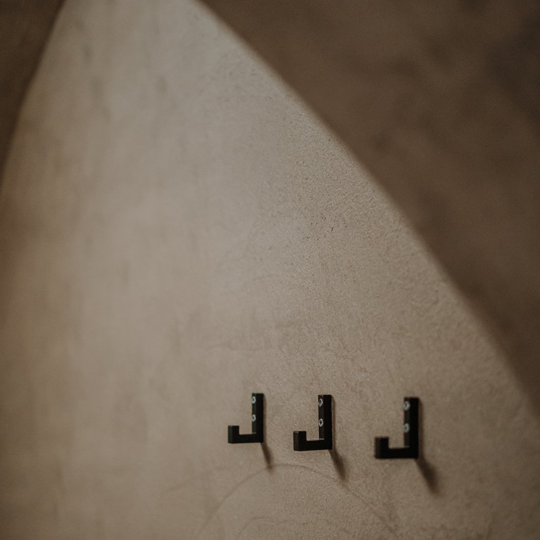 Three black wall hooks on a beige textured wall under an arch