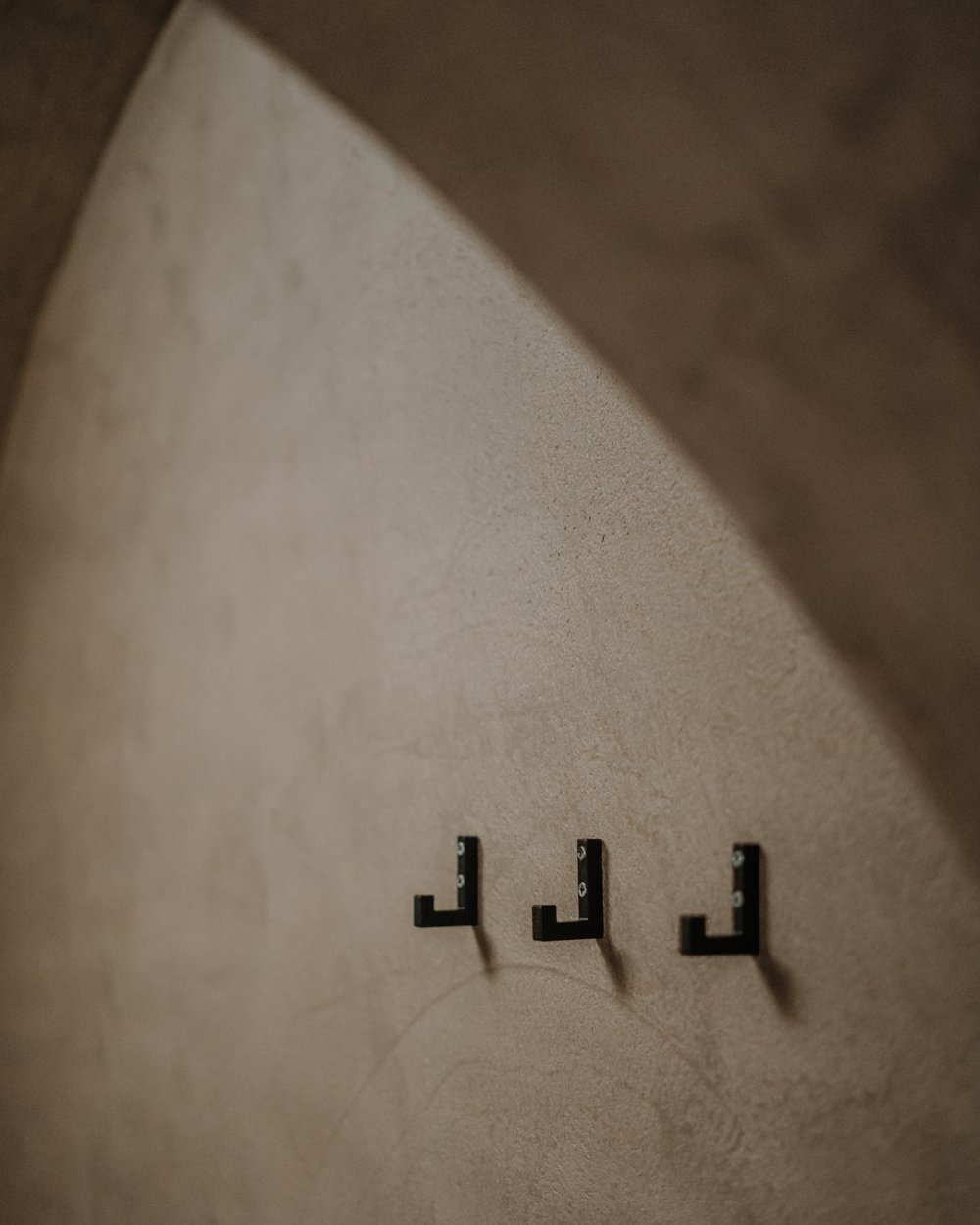 Drei schwarze Wandhaken auf beige strukturierter Wand unter einem Bogen