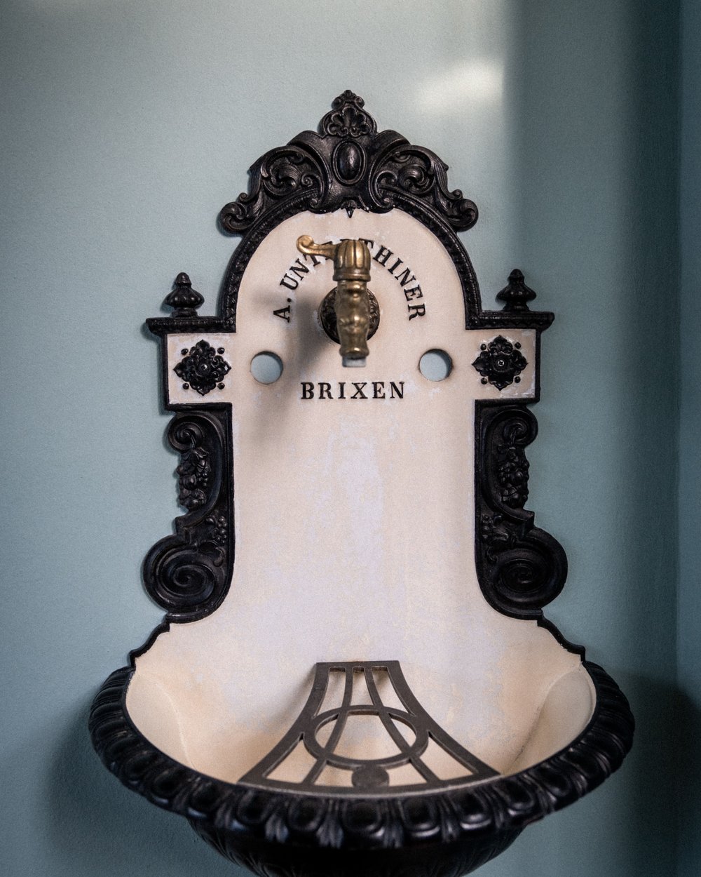 Antiker Wandbrunnen mit schwarzer Verzierung und goldfarbenem Wasserhahn