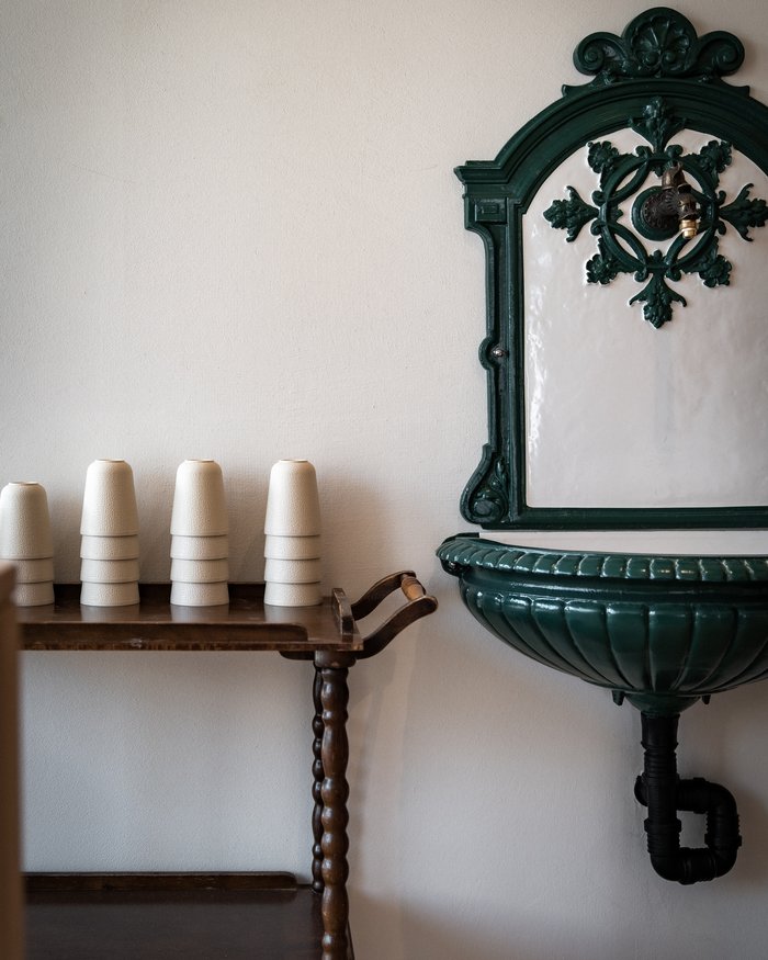 Antique green wall-mounted sink next to a wooden cart with white cups