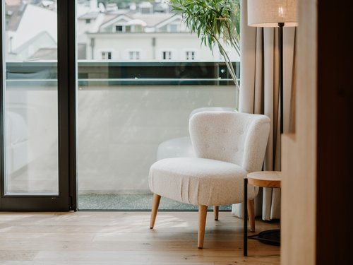 Light-colored chair next to floor lamp and large window overlooking buildings