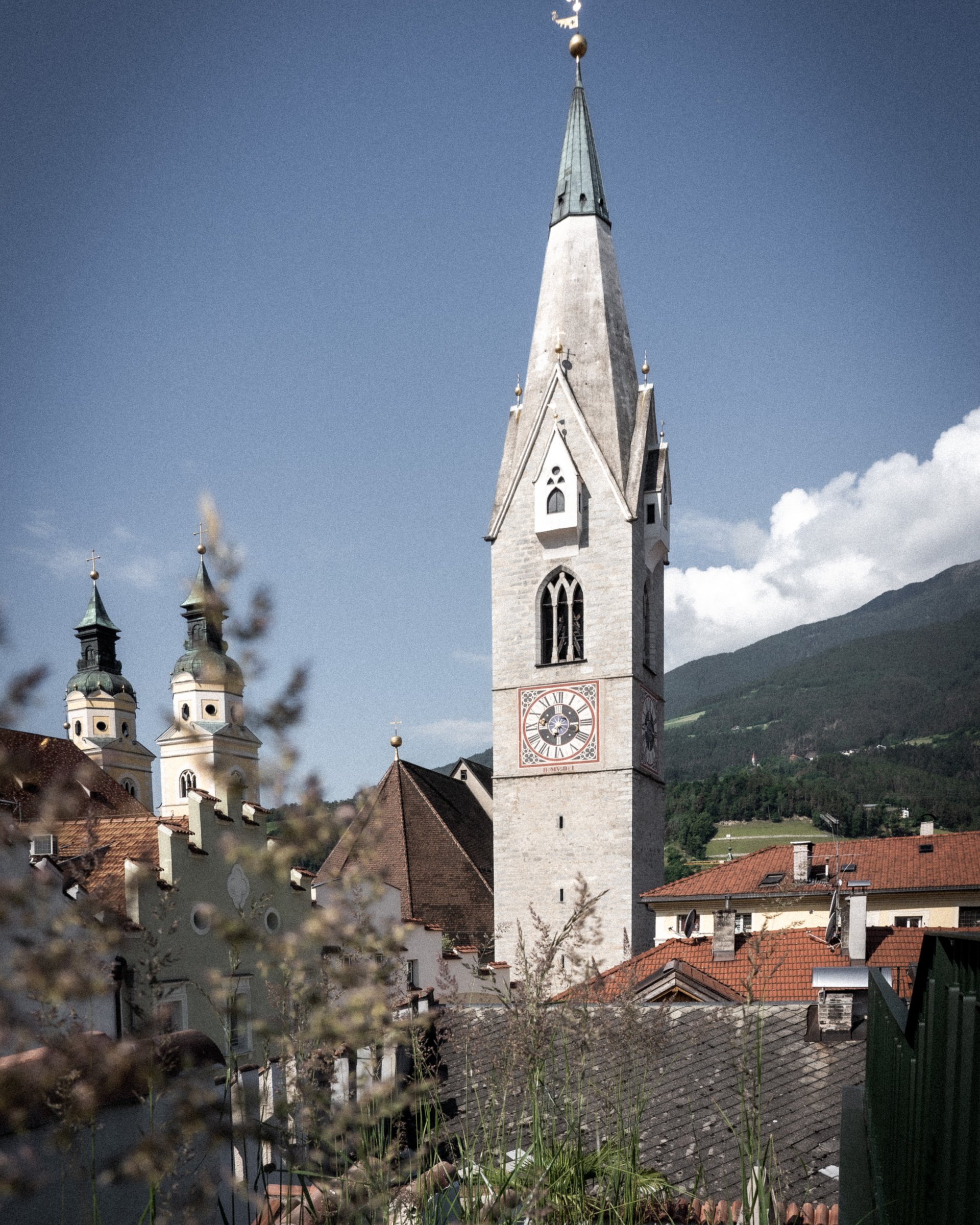 Kirchturm mit Uhr in einer Stadt vor bewaldeten Bergen