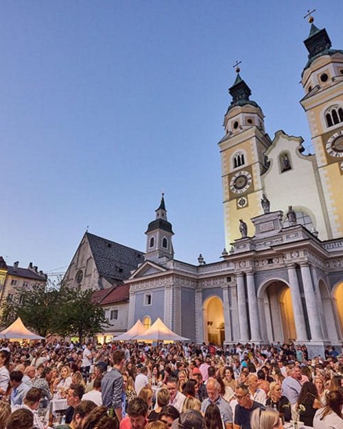 Menschenmenge bei einem Festival vor einer Kirche mit zwei Türmen bei Sonnenuntergang