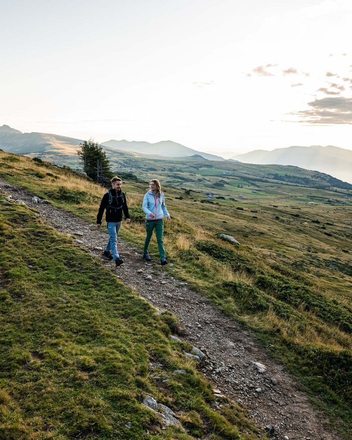 Zwei Wanderer auf Bergweg bei Sonnenaufgang mit Landschaft und Bergen
