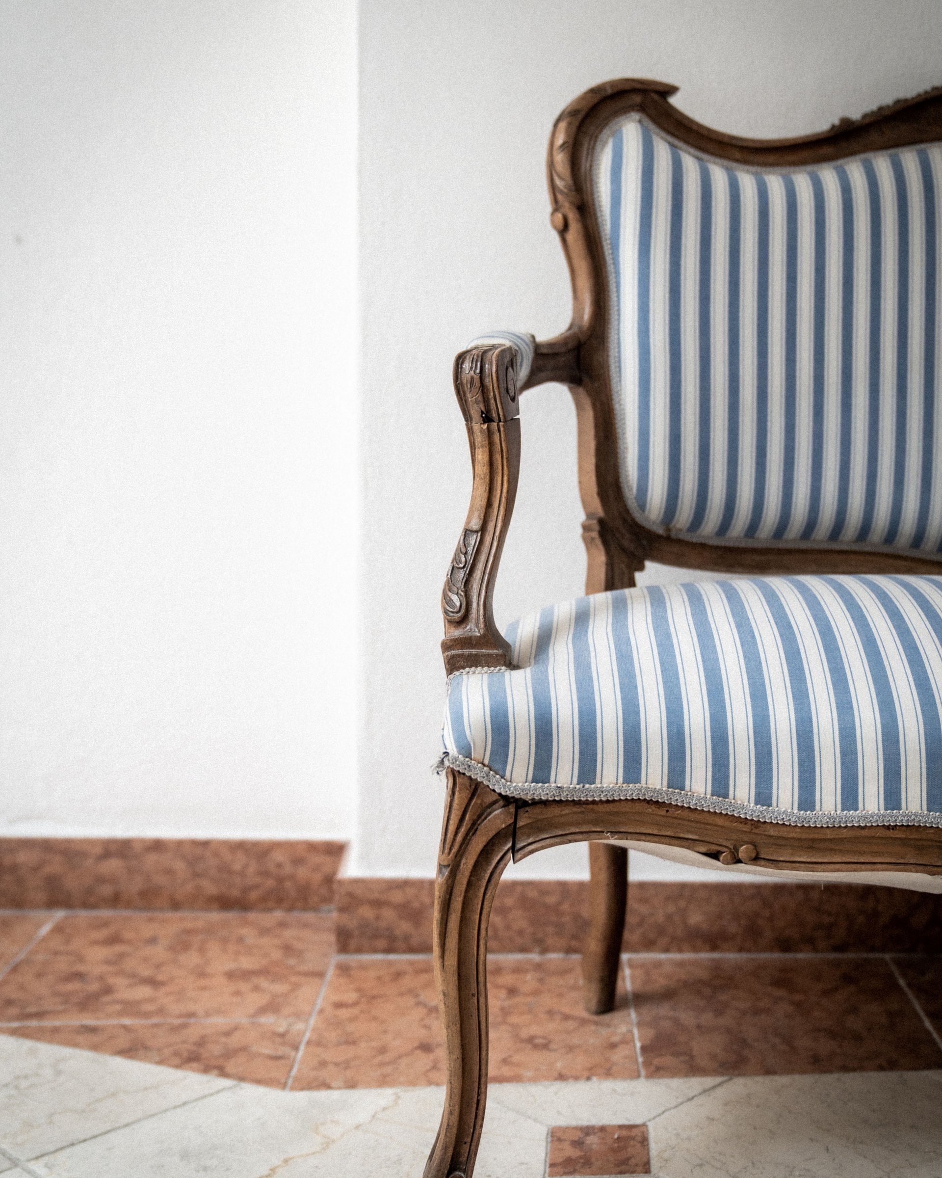 Antique wooden chair with blue and white striped upholstery against white wall