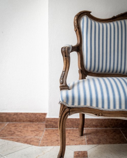 Antique wooden chair with blue and white striped upholstery against white wall