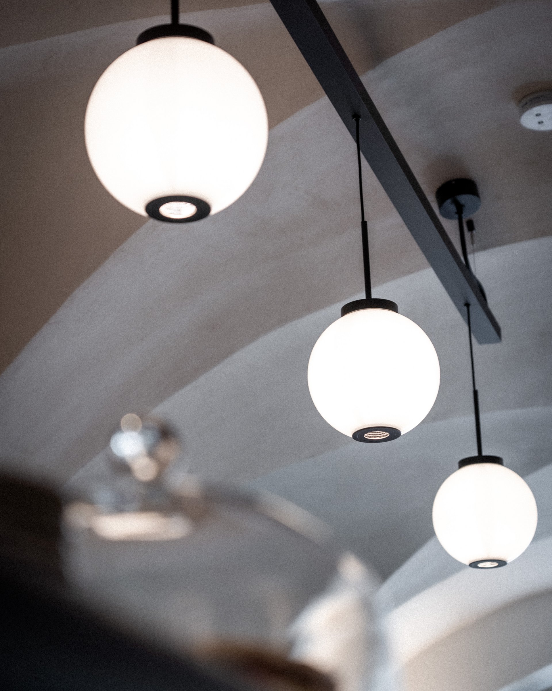 Drei runde, weiße Deckenlampen an einer schwarzen Stange