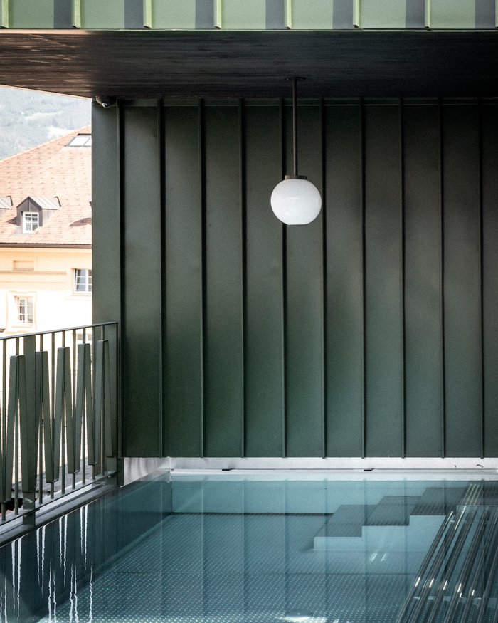 Modern pool with glass walls and single round lamp in green room