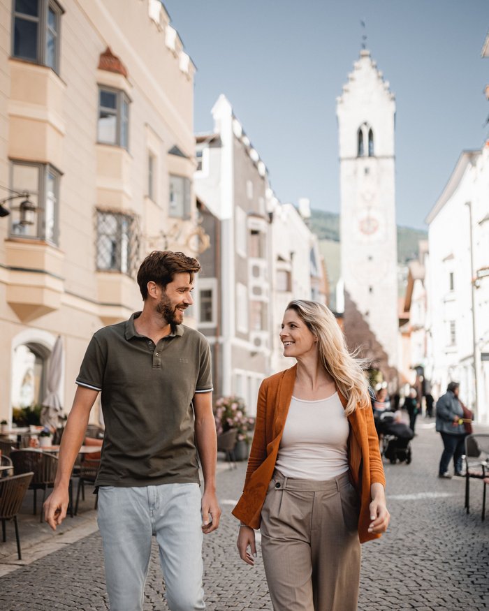 Couple walking and smiling in a cobblestone old town with a tower in the background