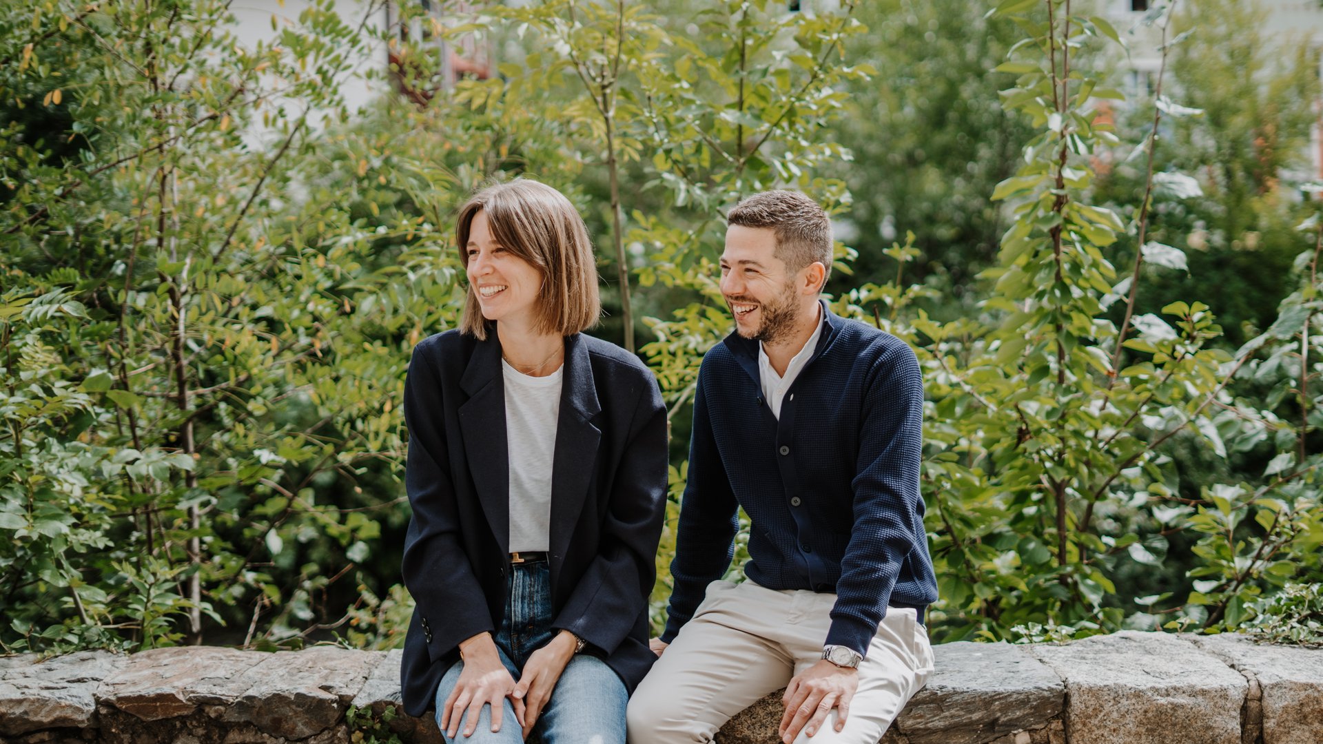 Young couple sitting and smiling on a stone wall in a garden
