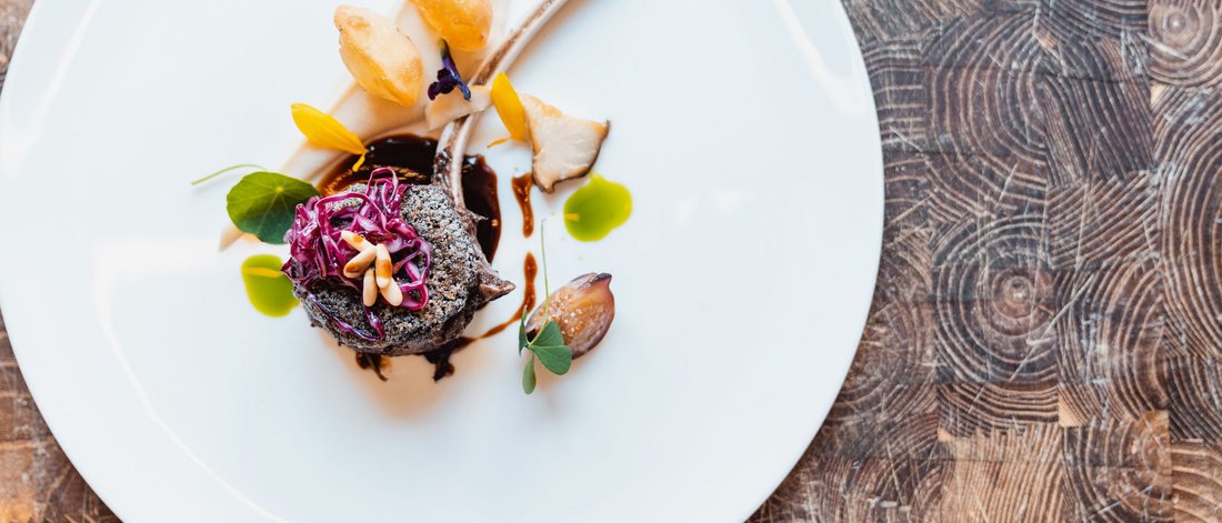 Elegantly plated gourmet dish with lamb chop and colorful garnishes on white plate