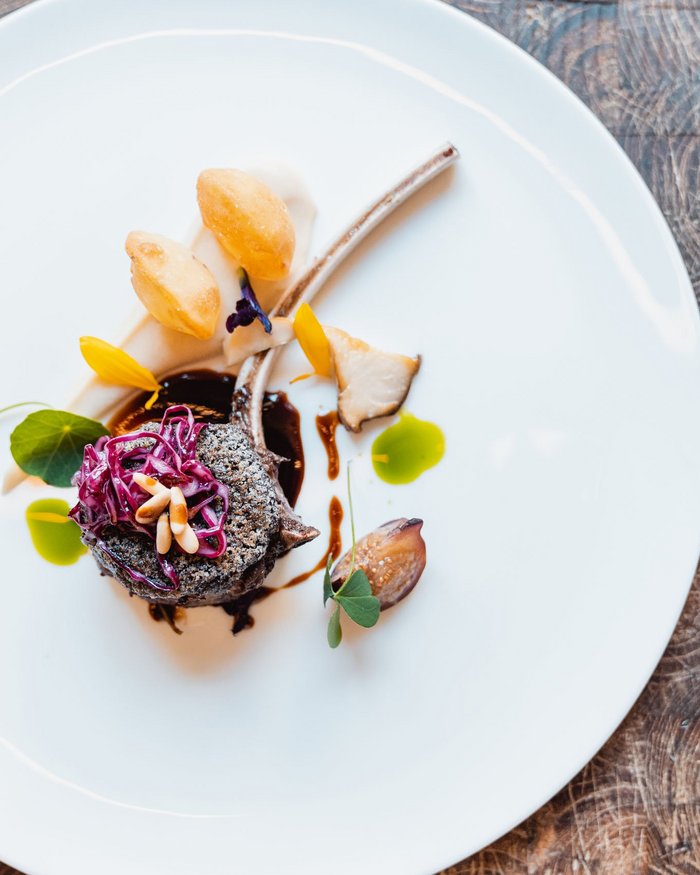 Elegantly plated gourmet dish with lamb chop and colorful garnishes on white plate