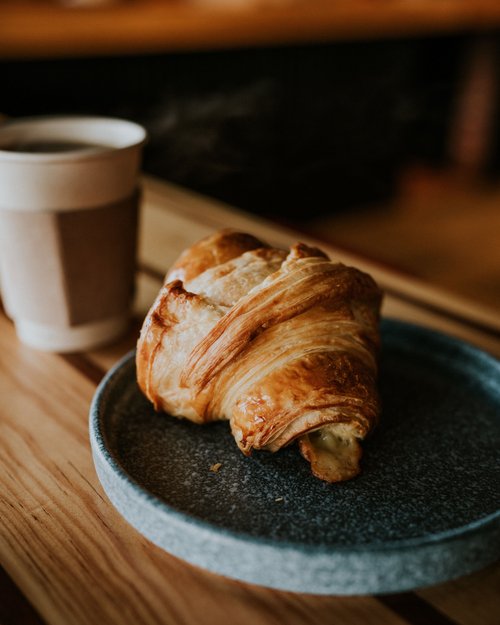 Frischer Croissant auf einem grauen Teller mit einem Kaffee im Hintergrund