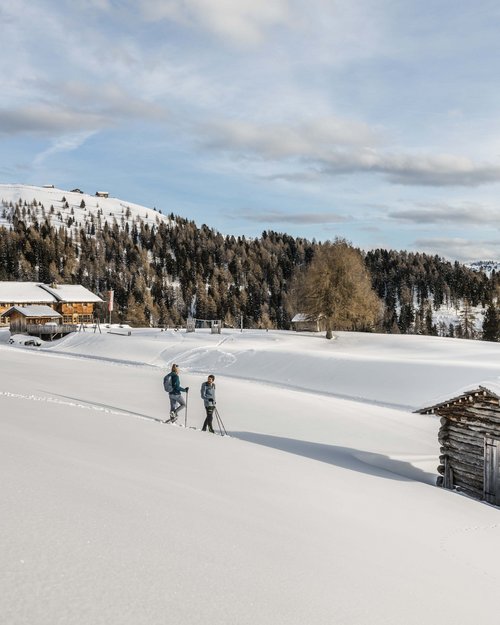 Zwei Menschen beim Schneeschuhwandern in verschneiter Berglandschaft mit Hütten