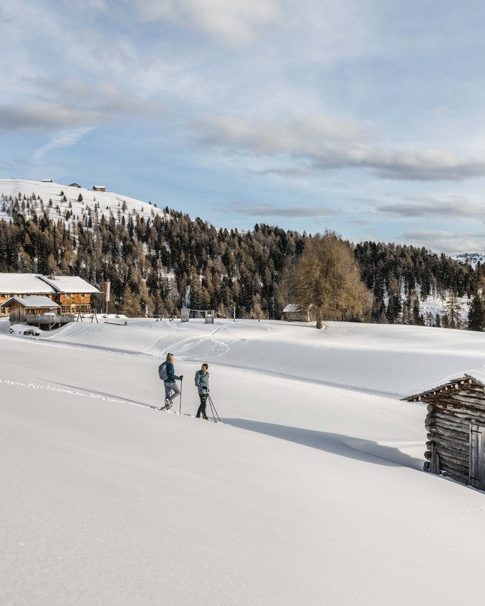Zwei Menschen beim Schneeschuhwandern in verschneiter Berglandschaft mit Hütten