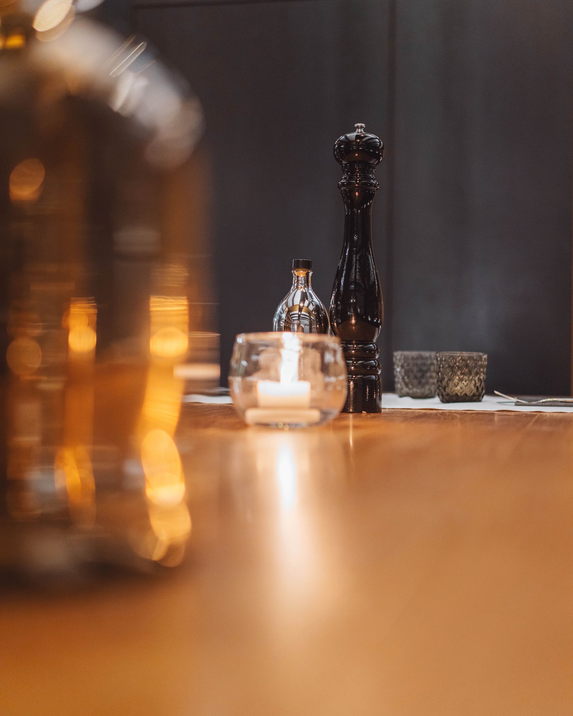 Black pepper grinder beside candle on wooden table in restaurant