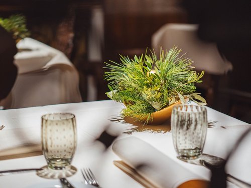 Tisch mit Tischdecke, Glas, Besteck und grünem Blumenschmuck