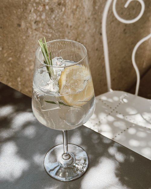 Glass with ice, lemon slice and rosemary sprig on metal table