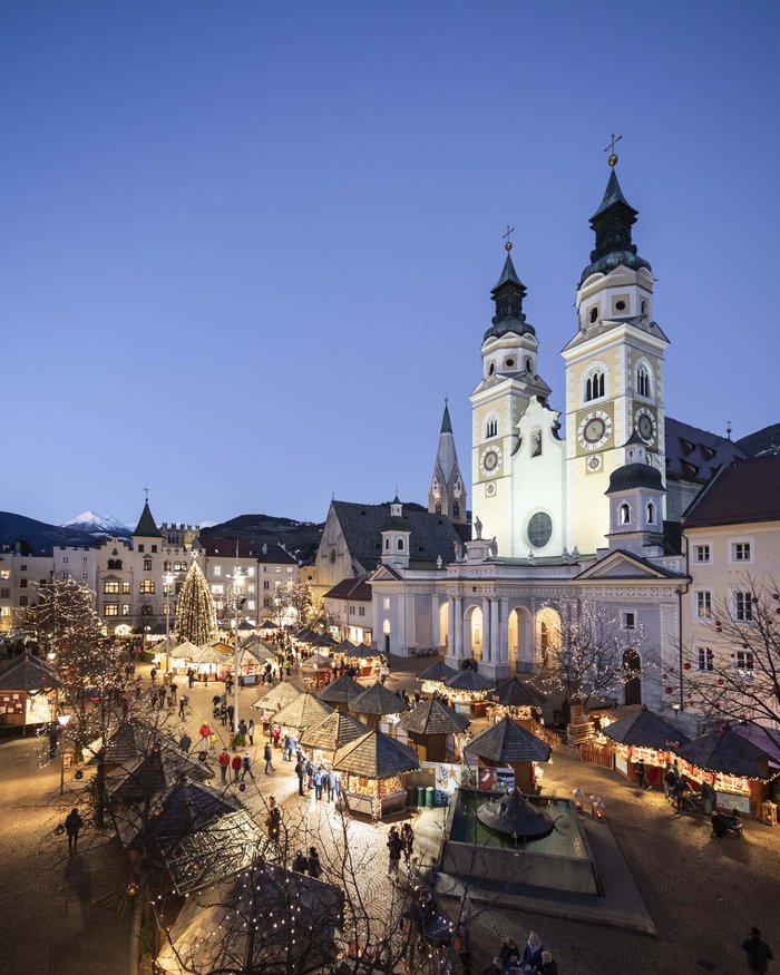 Christmas market with lit stalls and church at dusk