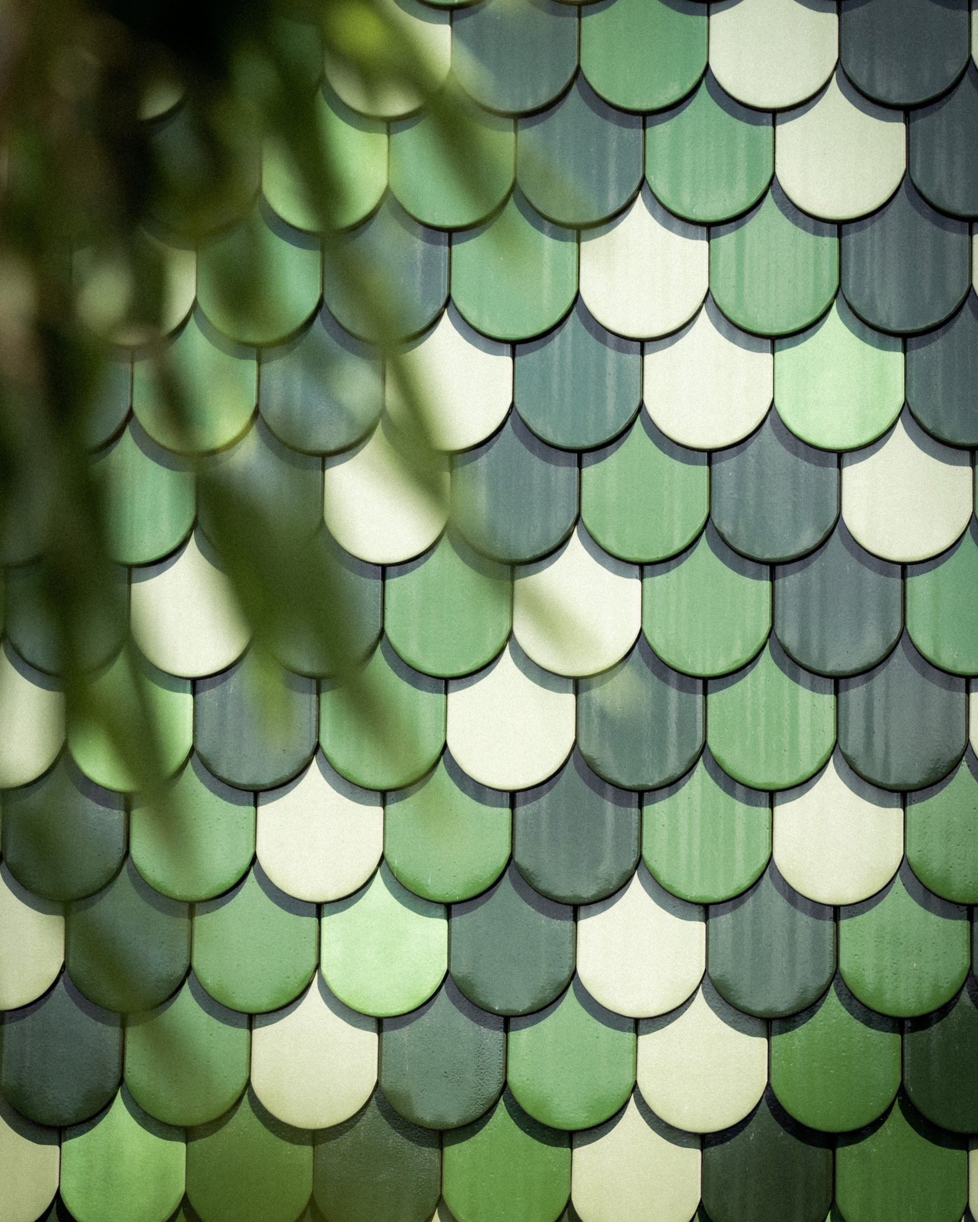 Grüne und weiße Schindeln in Fischschuppenmuster an einer Fassade