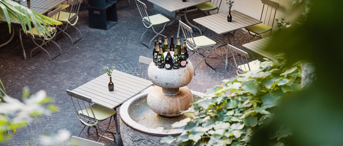 Empty outdoor café area with stone table and wine bottles on fountain