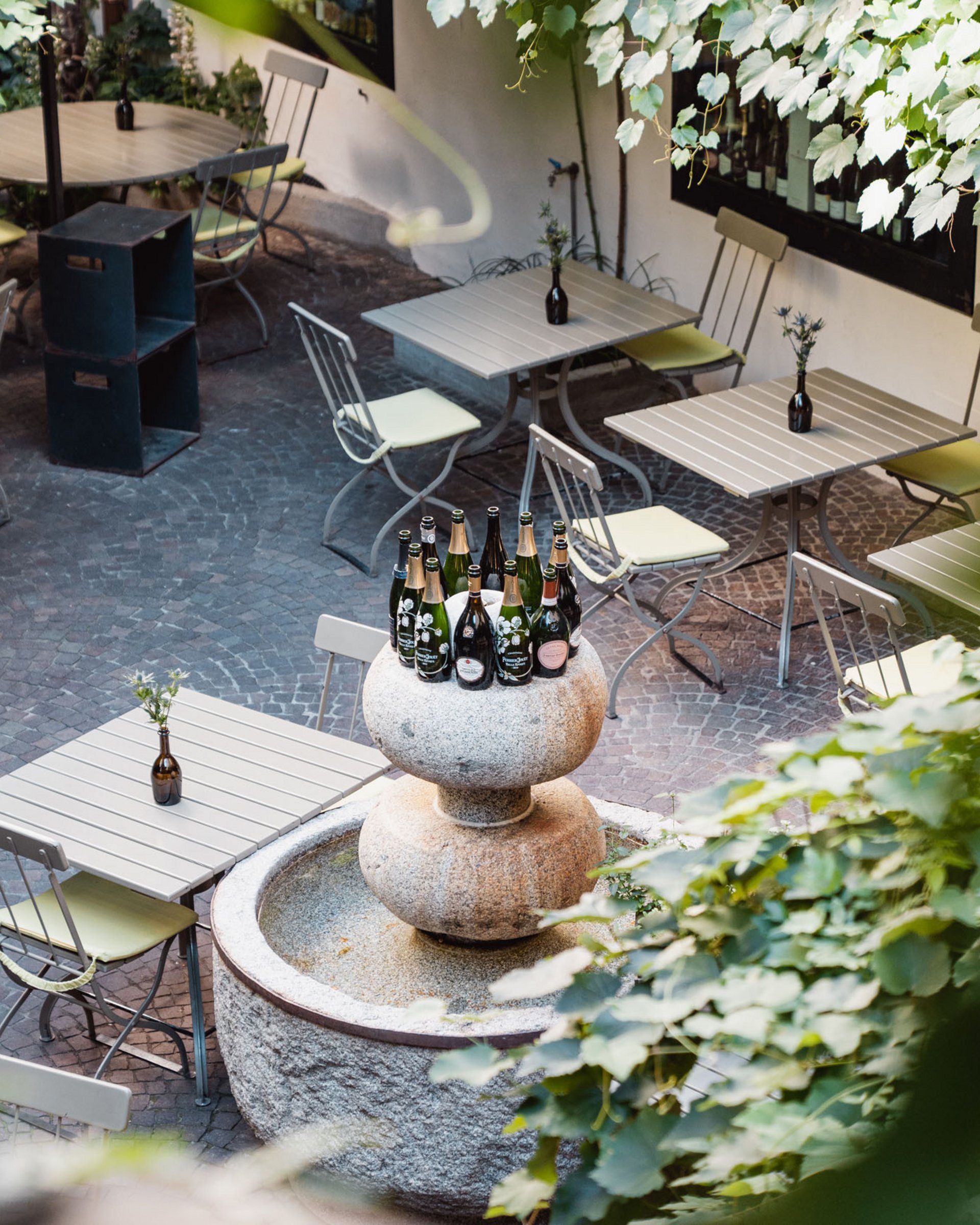 Empty outdoor café area with stone table and wine bottles on fountain