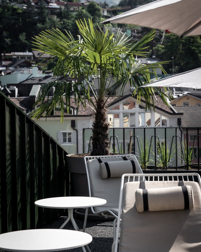 Terrace with lounge chairs, white tables, palm trees and mountains in the background