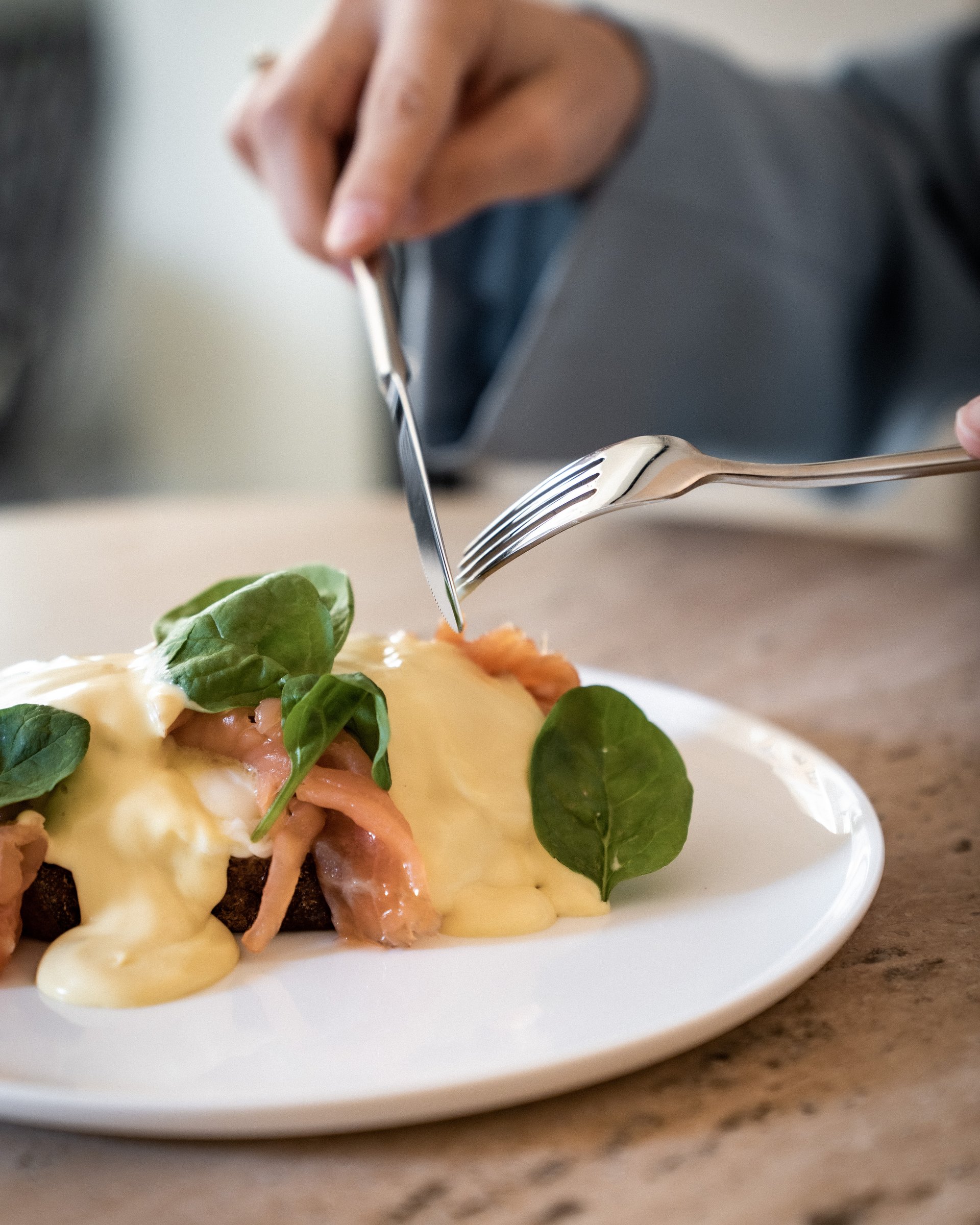Hand schneidet Lachs mit Sauce und Spinat auf Teller