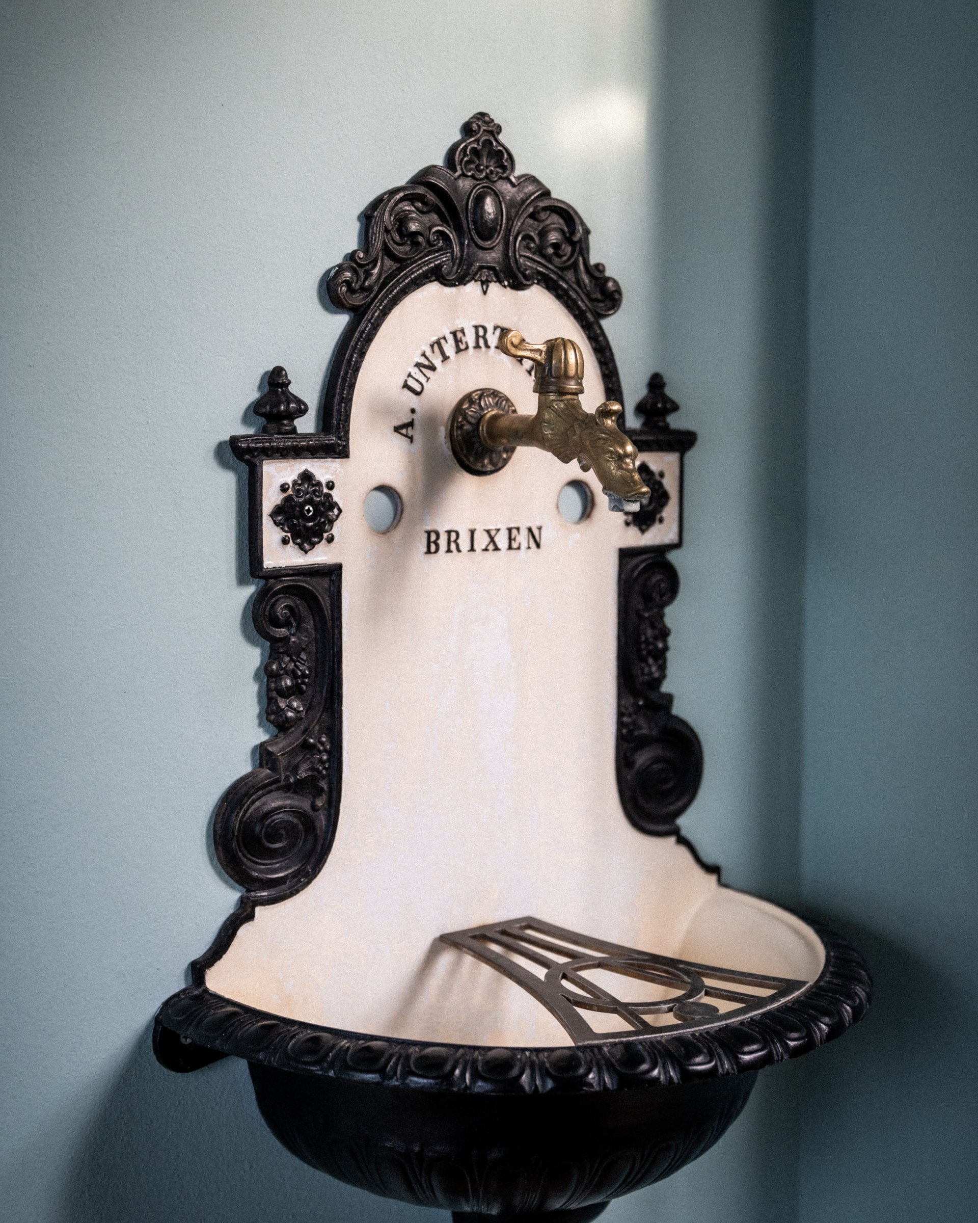 Antique wall fountain with ornate brass tap and Brixen inscription