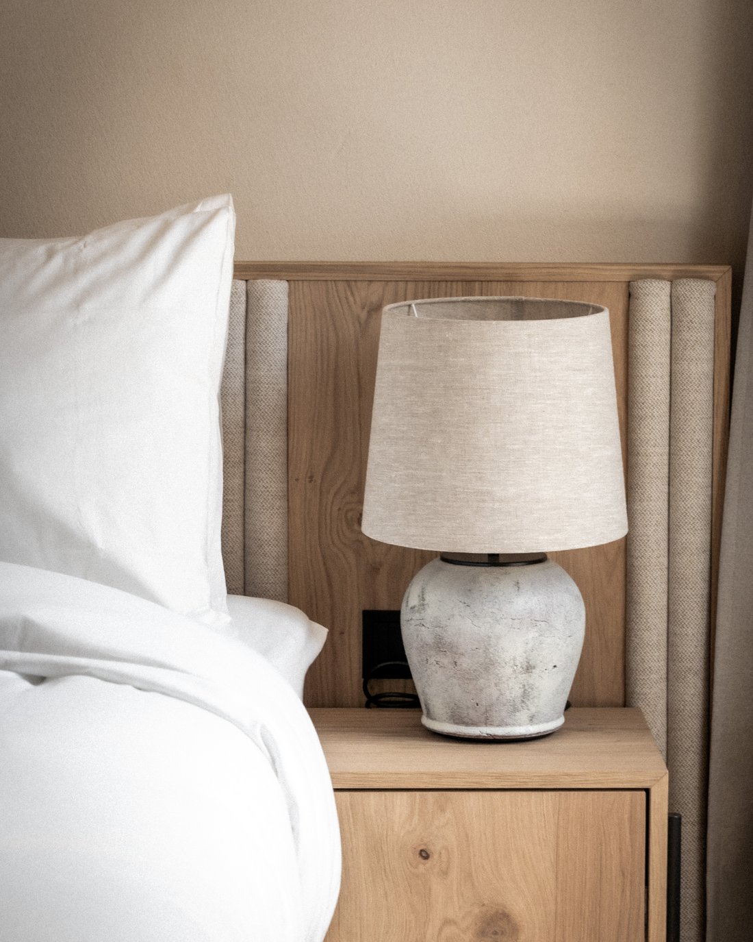 Nachttisch mit Lampe neben weißem Bett in neutralem Schlafzimmer