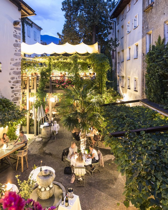 Abendliche Terrasse eines Restaurants mit Gästen und Pflanzen in einer Gasse